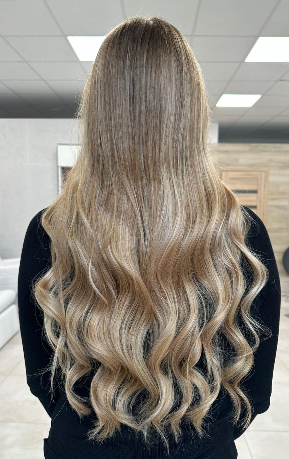 Długie, blond włosy z delikatnymi falami, widok z tyłu, oświetlenie studyjne, ukazujące subtelne refleksy i przejścia kolorystyczne na włosach.