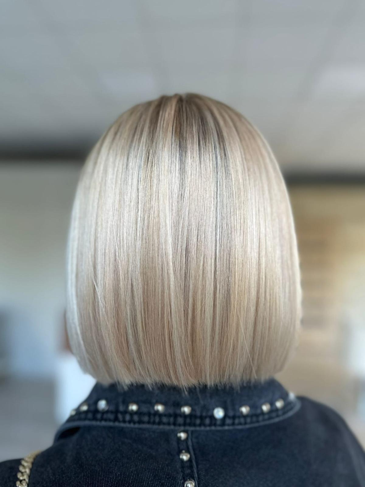 Tył głowy z krótkim, prostym bobem w odcieniach blondu, widoczna jeansowa kurtka z ozdobnymi nitami.