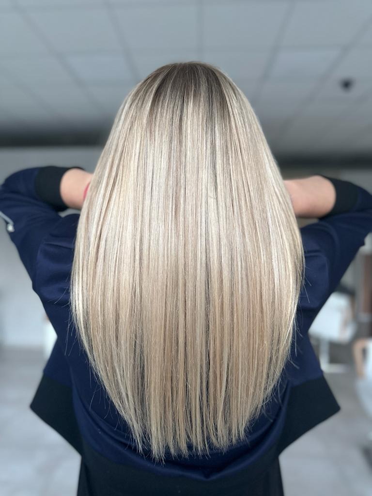 Długie, proste, blond włosy z ciemniejszym odrostem, ułożone na plecach, widok z tyłu, kobieta w granatowej bluzie.