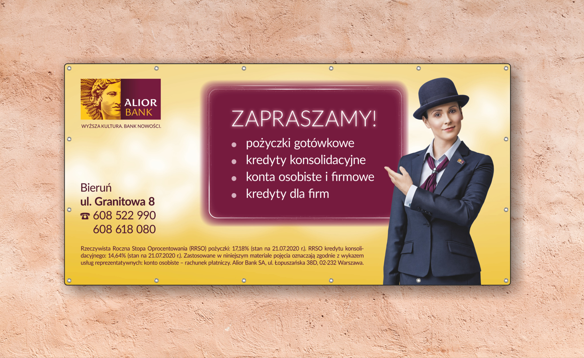 Banner reklamowy Alior Banku z wizerunkiem kobiety w garniturze i kapeluszu, oferujący pożyczki gotówkowe, kredyty konsolidacyjne, konta osobiste i firmowe oraz kredyty dla firm, zawieszony...