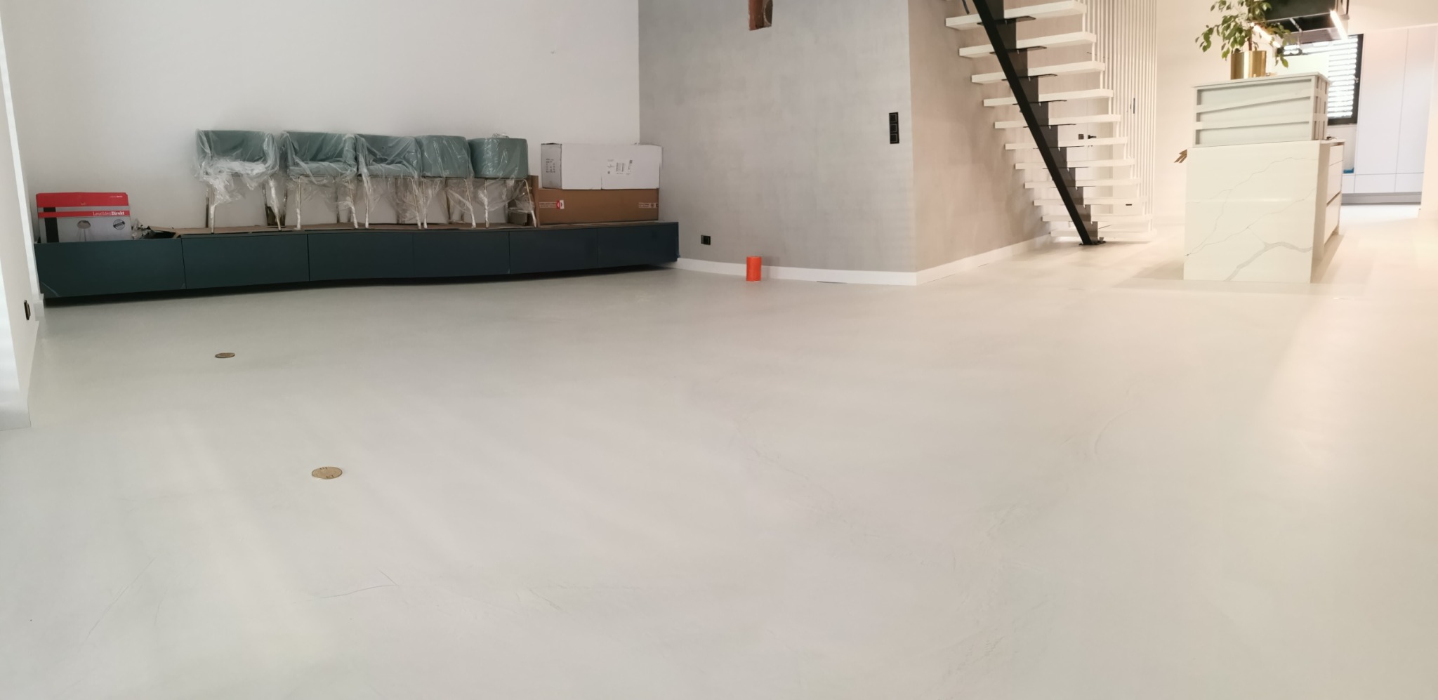 Jasna, jednolita podłoga w przestronnym wnętrzu z nowoczesnymi schodami i wyspą kuchenną. Krzesła w folii ochronnej i kartony stoją pod ścianą.