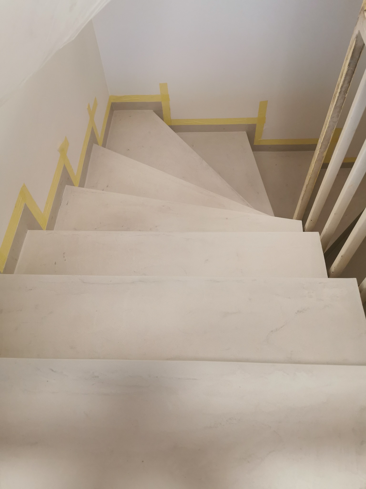 Betonowe schody wewnętrzne w trakcie prac wykończeniowych, zabezpieczone taśmą malarską przy ścianie, widok z góry na stopnie i fragment balustrady.