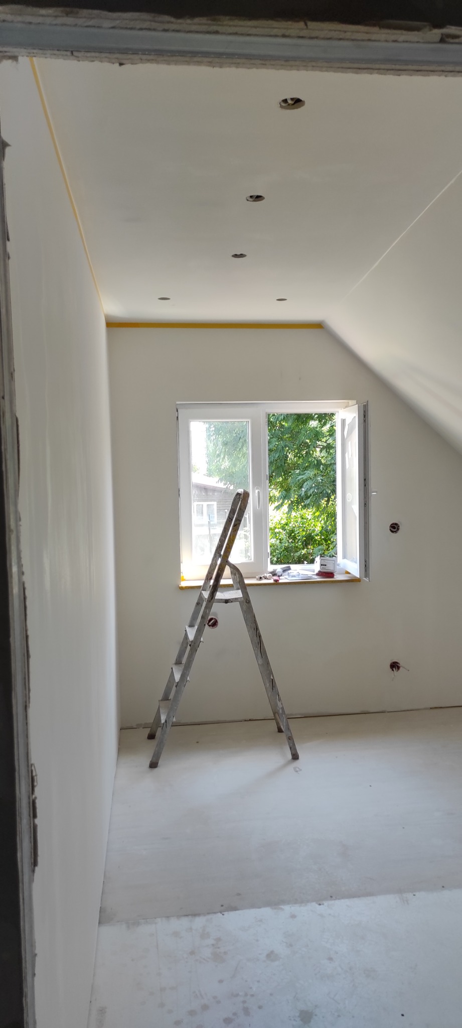 Pokój w trakcie remontu, ściany przygotowane do malowania, zabezpieczone taśmą, aluminiowa drabina oparta o parapet okna.