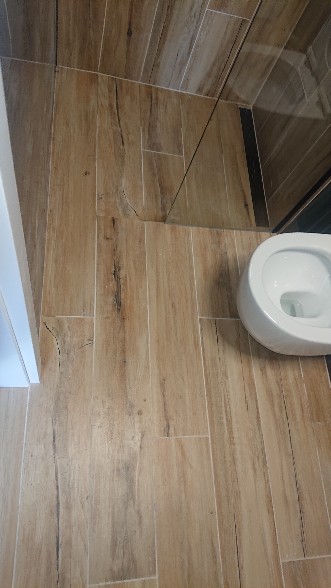 Ułożone płytki imitujące drewno na podłodze i ścianie w łazience w Boguszynku, widoczna muszla klozetowa i fragment kabiny prysznicowej.