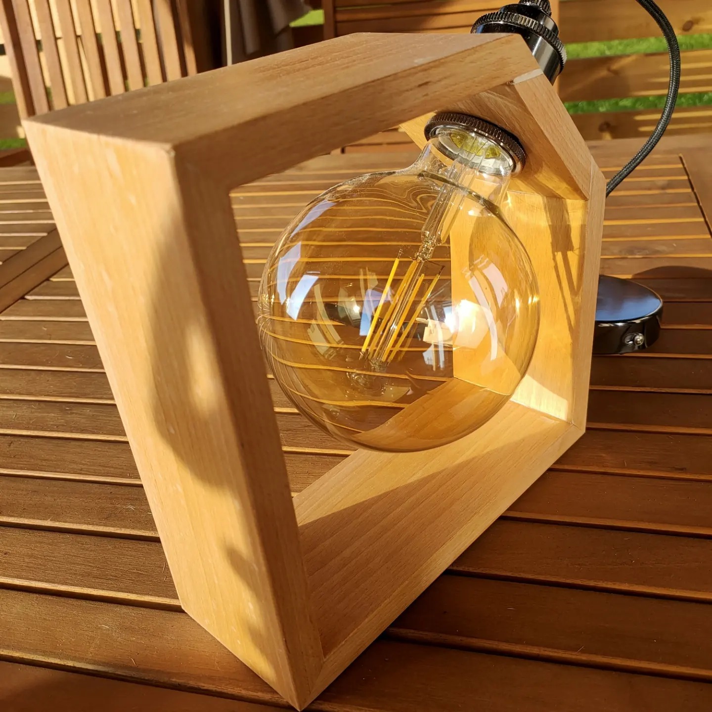 Drewniana lampka nocna z żarówką w stylu retro, ustawiona na drewnianym stole ogrodowym.