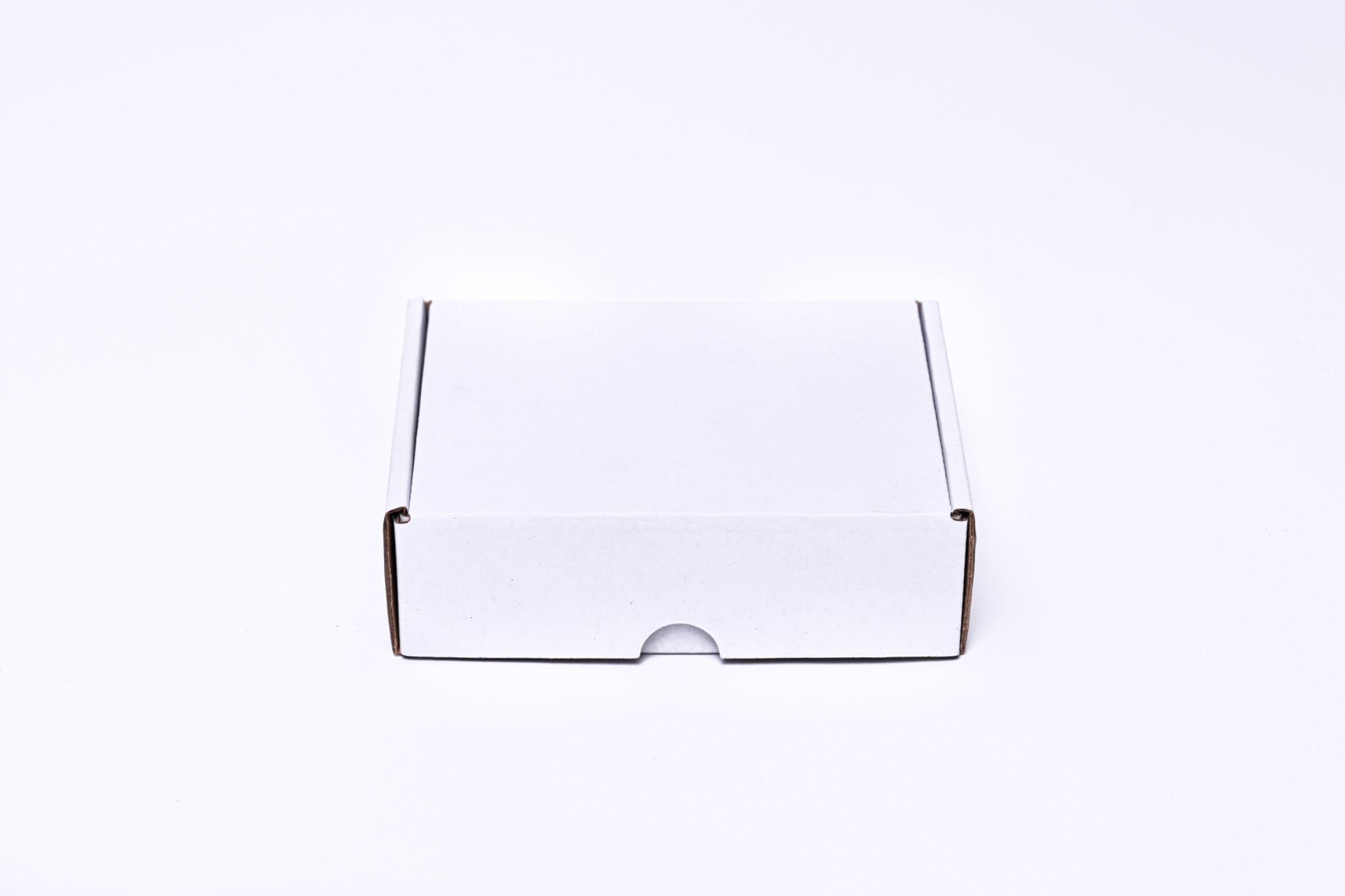 Pudełko z białej tektury, zamknięte, z wycięciem na palec u dołu, na białym tle.