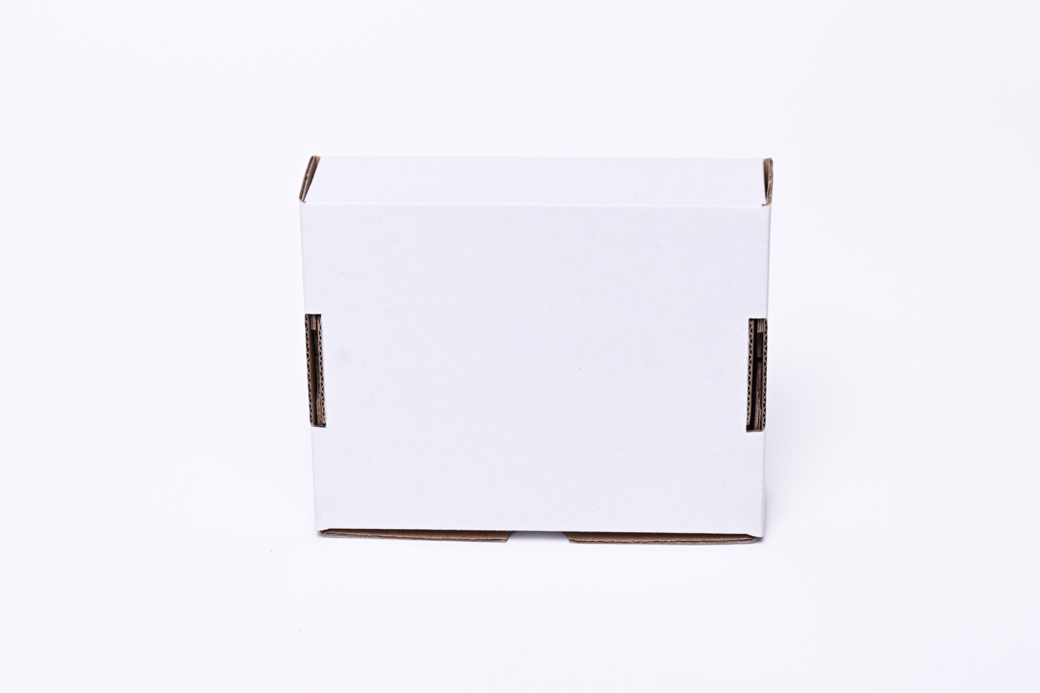Białe, kartonowe pudełko z widocznymi brązowymi krawędziami i wycięciami na klapy, ustawione centralnie na białym tle.