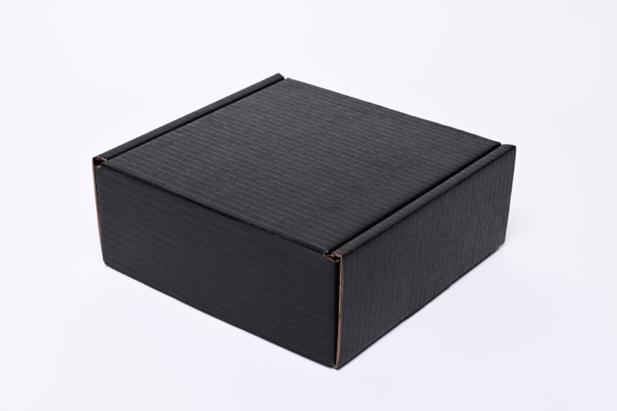 Czarny, kwadratowy karton z tektury falistej, zamknięty, widoczny pod kątem na białym tle.