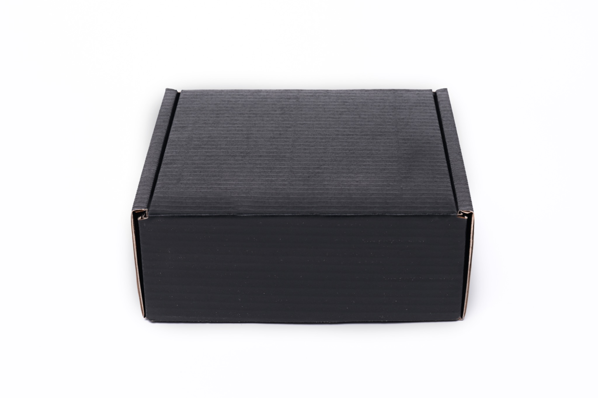 Zamknięte, czarne, tekturowe pudełko z widoczną teksturą w postaci drobnych, poziomych prążków, umieszczone centralnie na białym tle.