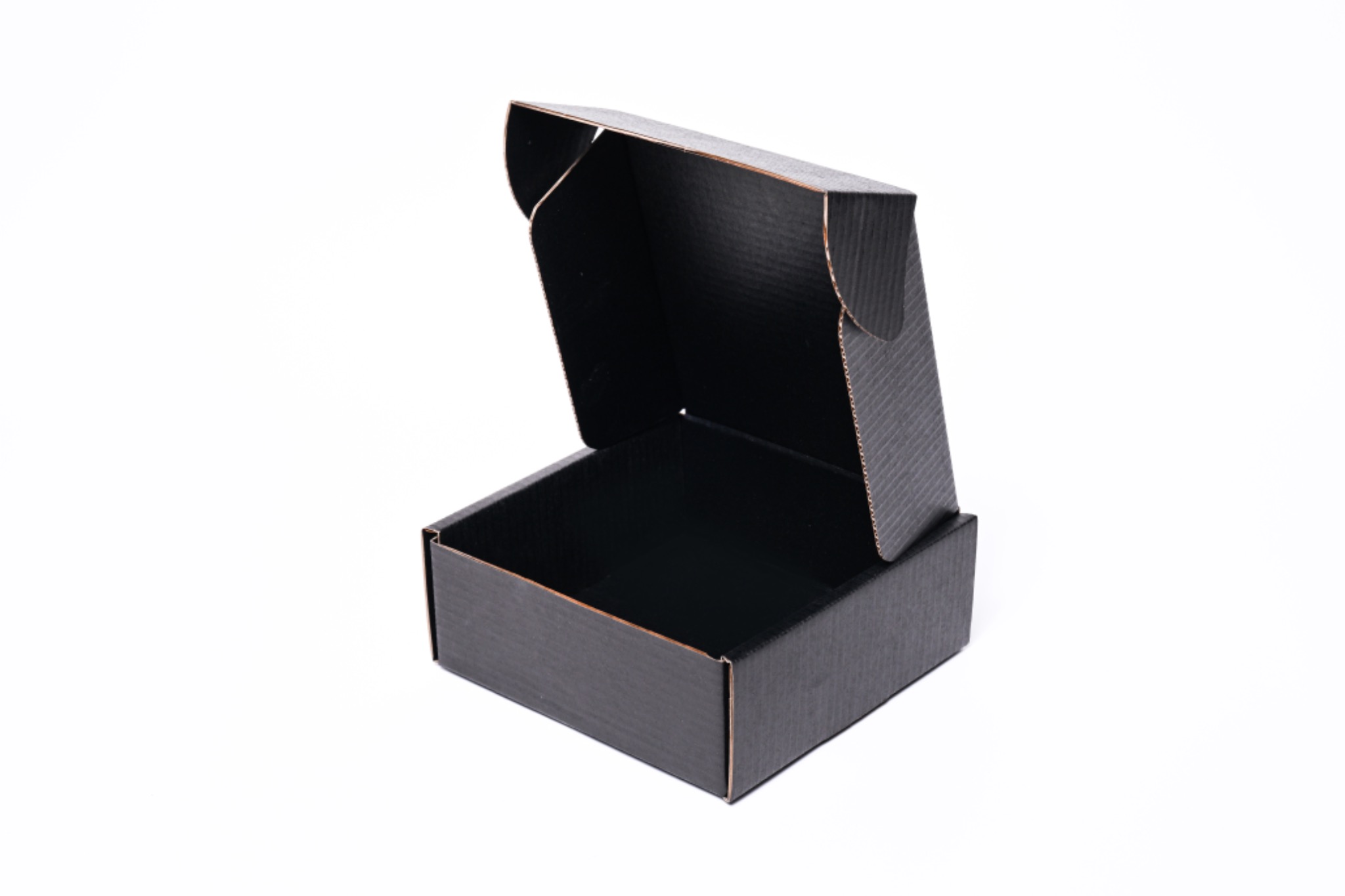 Otwarta, pusta, czarna, tekturowa skrzynka klapowa na białym tle, widoczna faktura tektury.