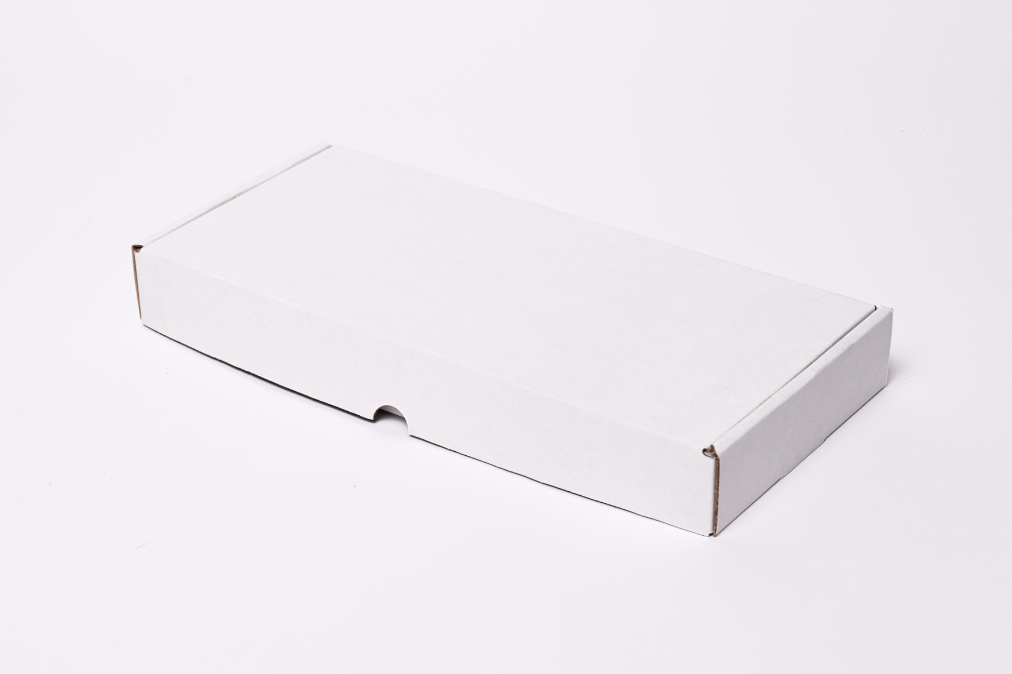 Pudełko z białej tektury, widoczne delikatne wycięcie ułatwiające otwieranie, leżące na białym tle pod kątem.