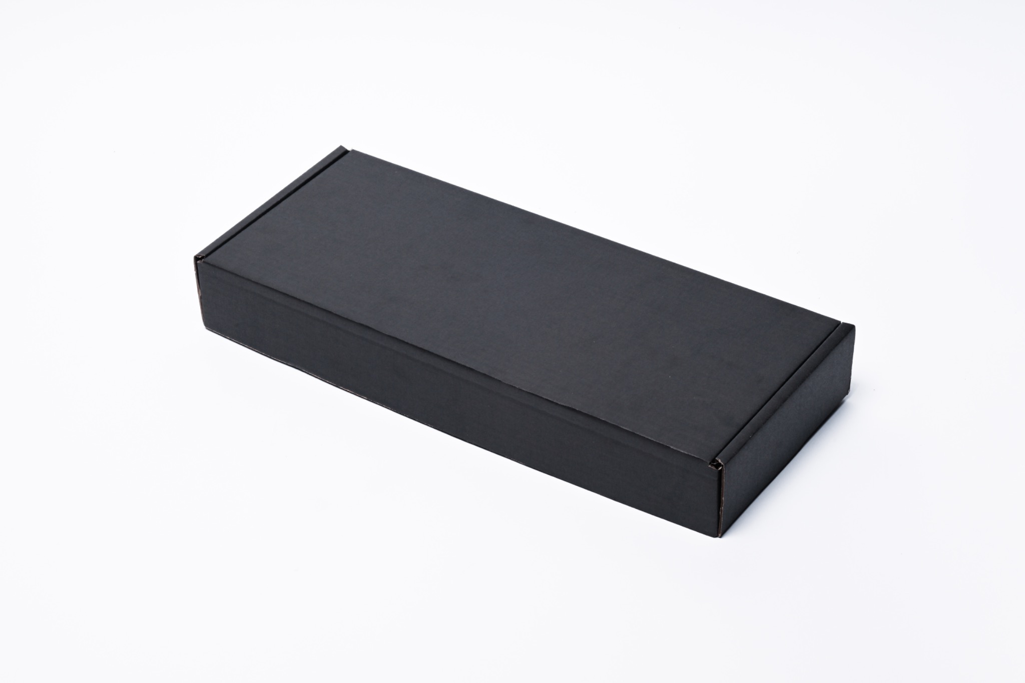 Pudełko kartonowe w kolorze czarnym, leżące na białym tle, dostarczone przez firmę z Grudziądza. Minimalistyczny design opakowania.