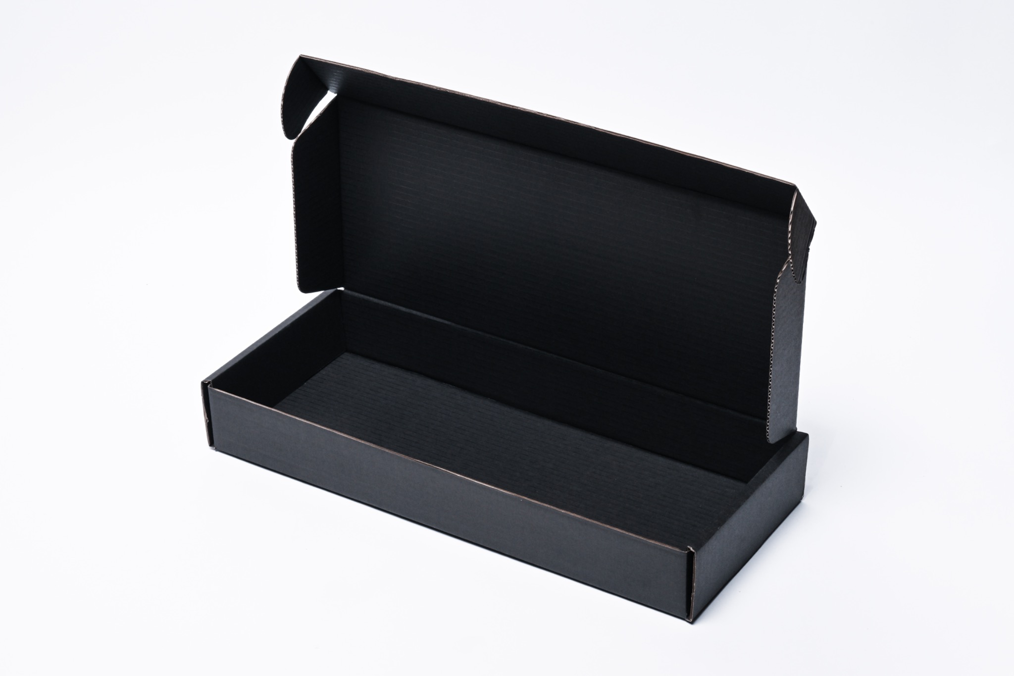 Otwarta, pusta, czarna, tekturowa skrzynka z widoczną fakturą tektury wewnątrz, na białym tle.