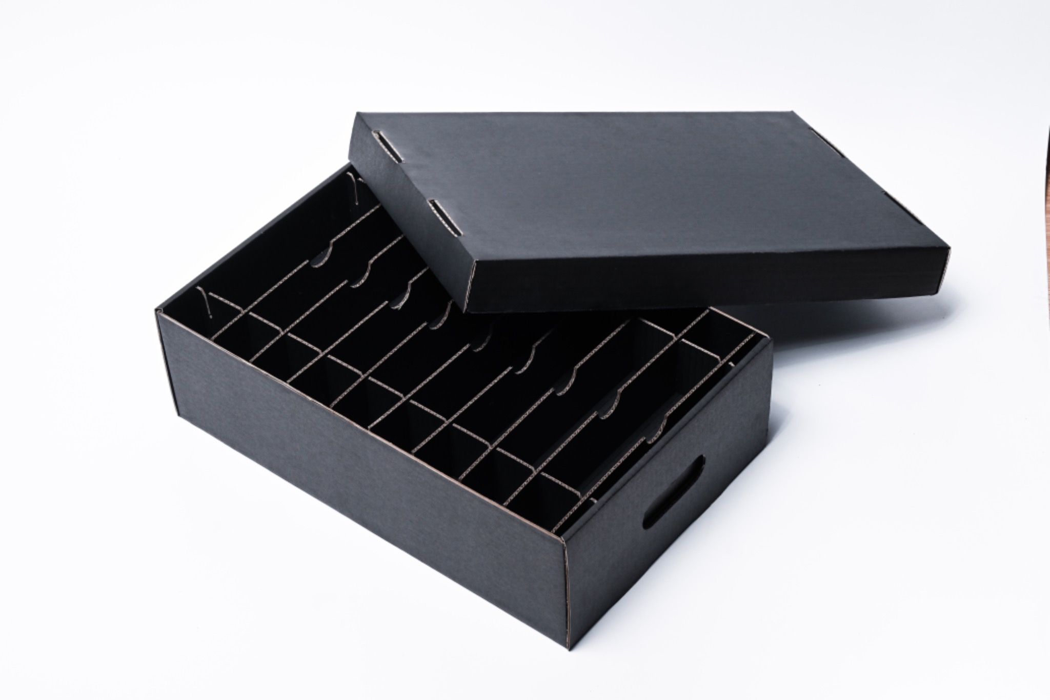 Czarne, kartonowe pudełko z przegródkami i uchwytami, z pokrywką leżącą obok, na białym tle.