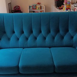 Mateusz Stenzel - Turkusowa sofa trzyosobowa z pikowanym oparciem w salonie, widoczne zabawki dziecięce w tle.