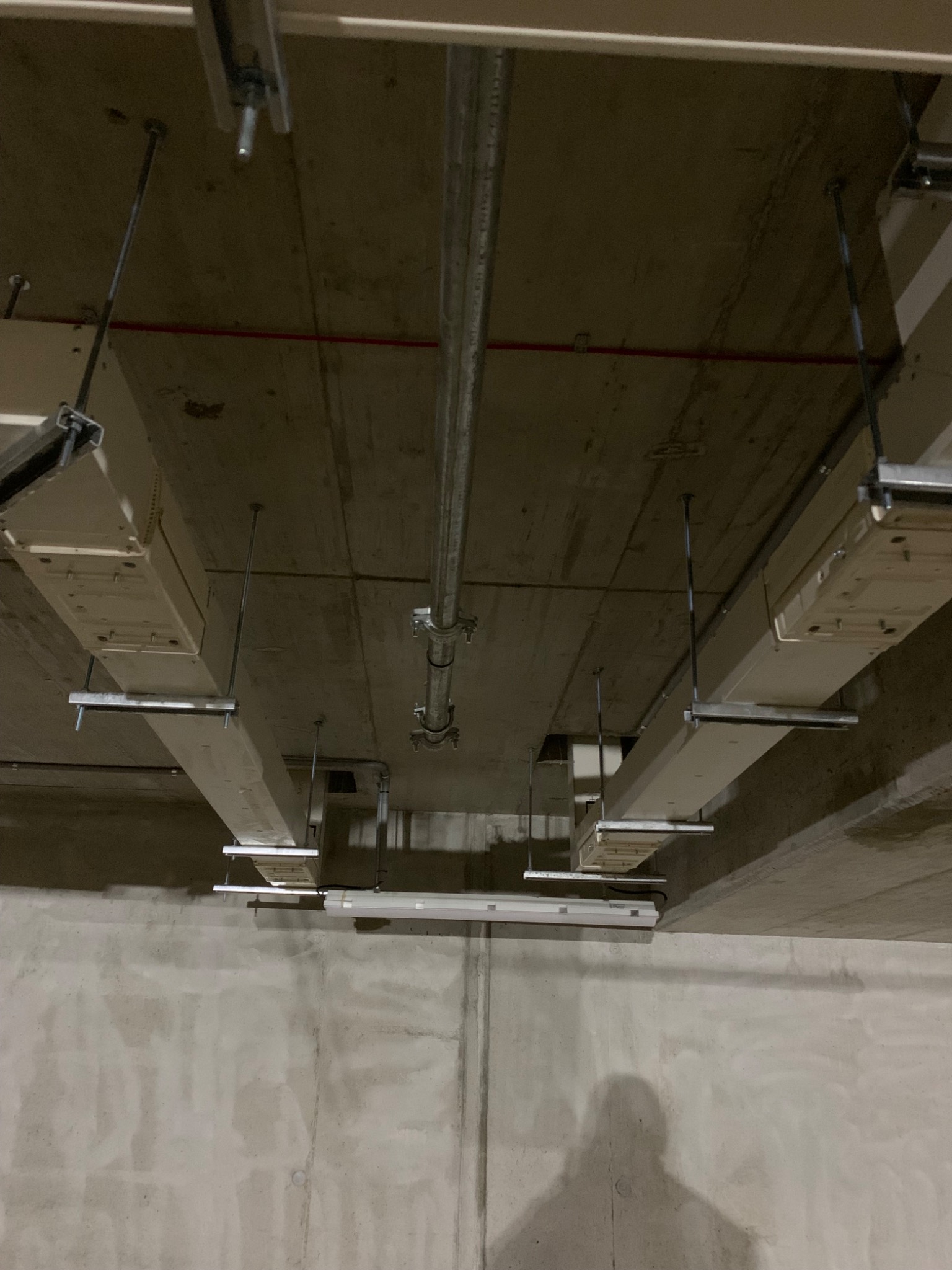 Widok sufitu z zamontowanymi elementami instalacji, widoczne rury, kable i profile mocujące, surowy betonowy strop i ściana w tle.