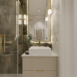Jotem Studio - Nowoczesna łazienka z kabiną prysznicową, umywalką nablatową i podświetlanym lustrem w złotej ramie. Na blacie szczotka do włosów i dozownik mydła. Ściany wykończone płytkami imitującymi marmur...