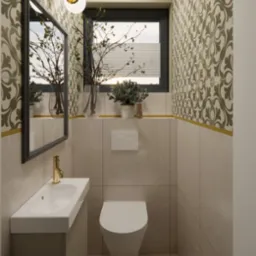 Kompaktowa łazienka z beżowymi płytkami, wzorzystą tapetą i złotymi akcentami, wisząca toaleta, umywalka z szafką, lustro w czarnej ramie i dekoracyjne gałązki w wazonie.