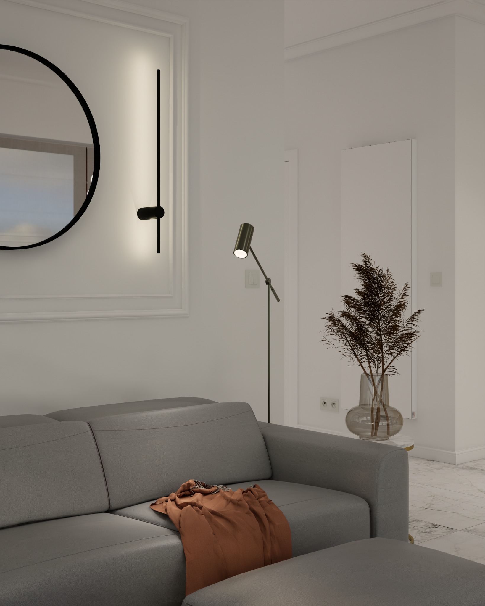 Minimalistyczny salon z szarą sofą, okrągłym lustrem i lampą podłogową, uzupełniony dekoracyjną trawą w szklanym wazonie.