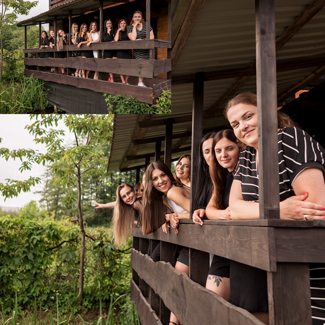 Grupa uśmiechniętych młodych kobiet pozuje na drewnianym tarasie domku letniskowego, część z nich wystaje zza balustrady, na zewnątrz widoczna zieleń.
