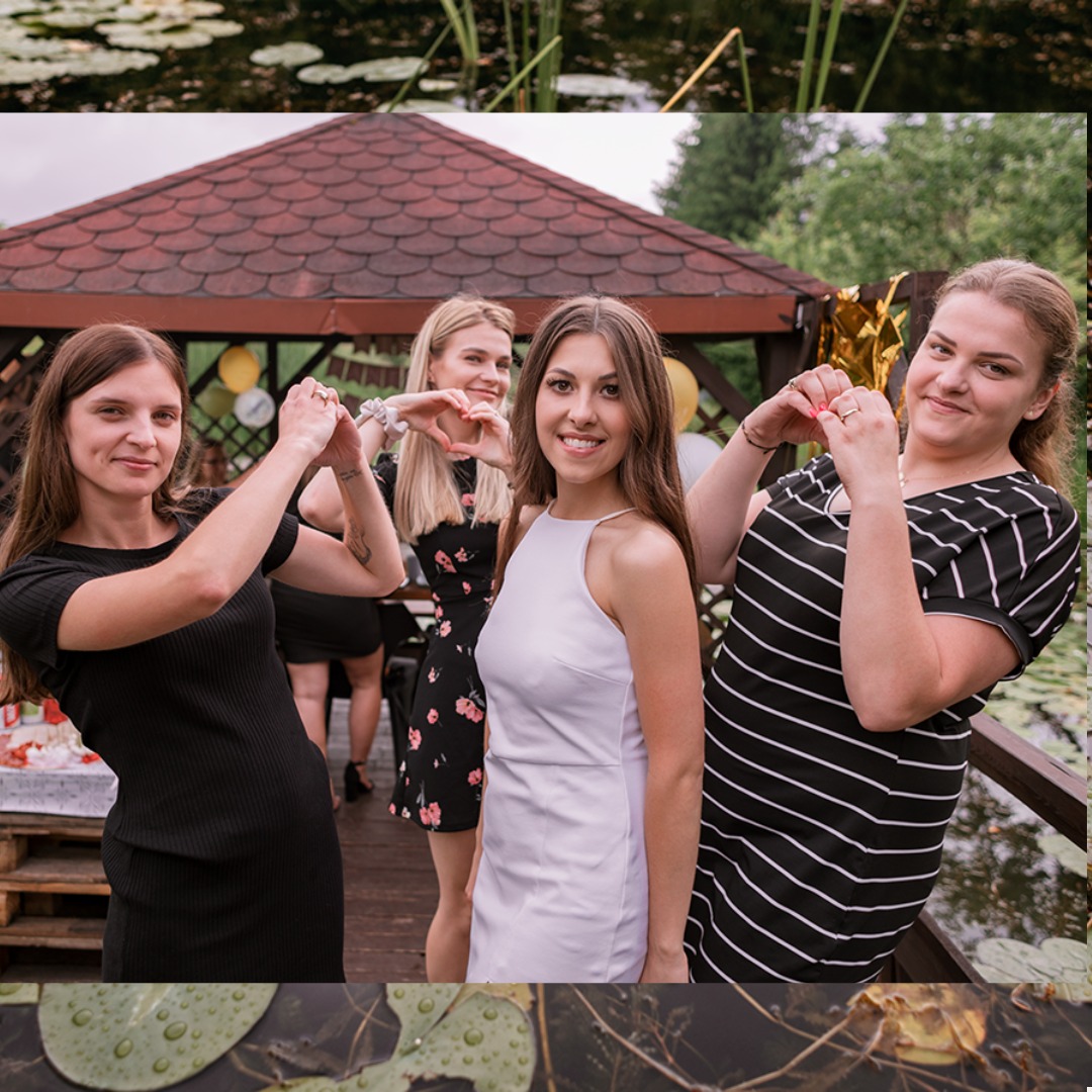 Cztery uśmiechnięte kobiety pozują na drewnianym pomoście, tworząc dłońmi kształt serca, w tle altana z balonami i staw z liliami wodnymi.