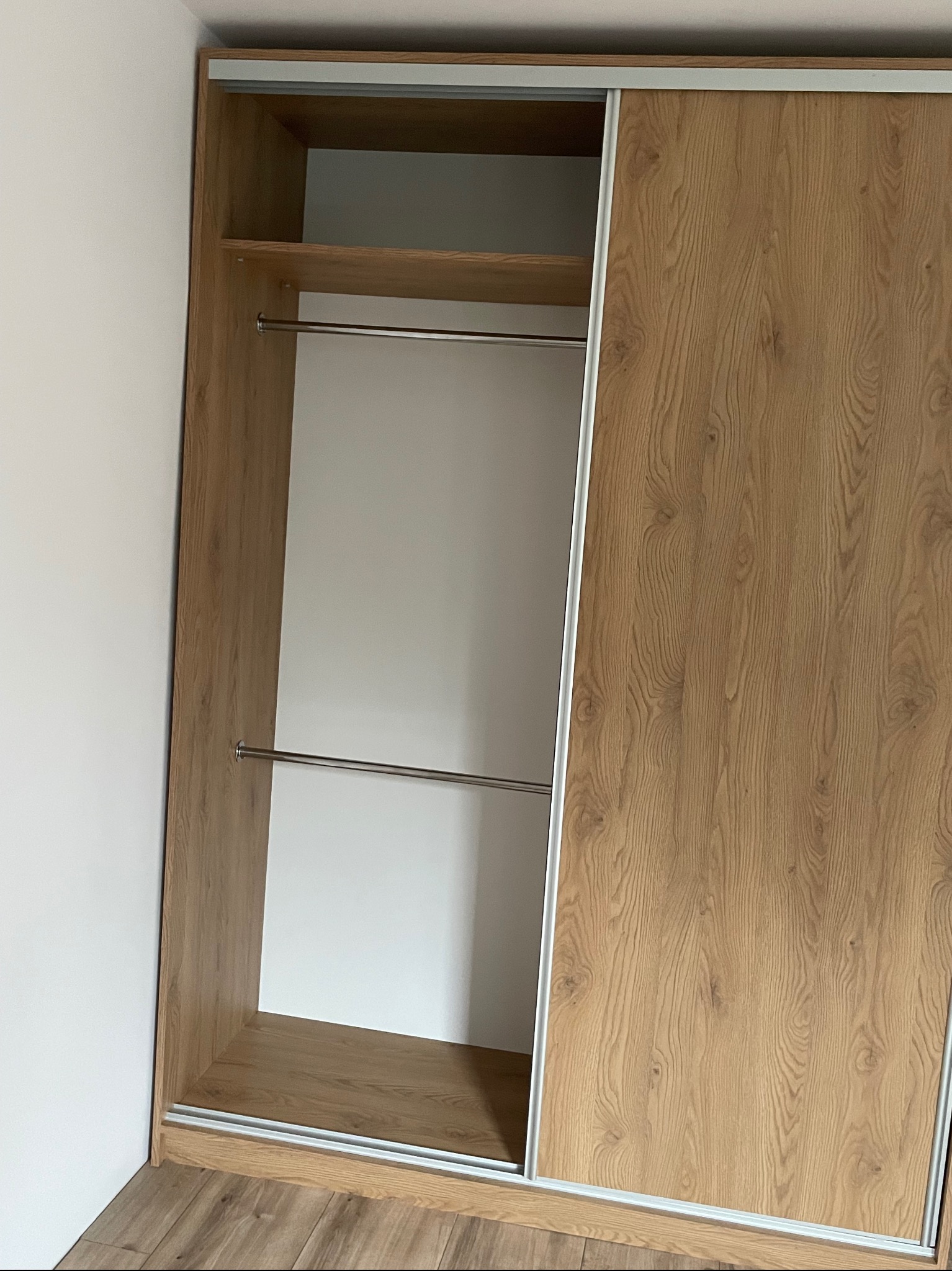 Wnętrze szafy z przesuwnymi drzwiami o drewnianym wykończeniu, widoczne półki i drążki na ubrania, bez zawartości, z bliska