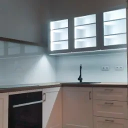 Nowoczesna, jasna kuchnia z białymi szafkami, drewnianym blatem, szklanym panelem nad blatem i oświetleniem LED pod szafkami wiszącymi.