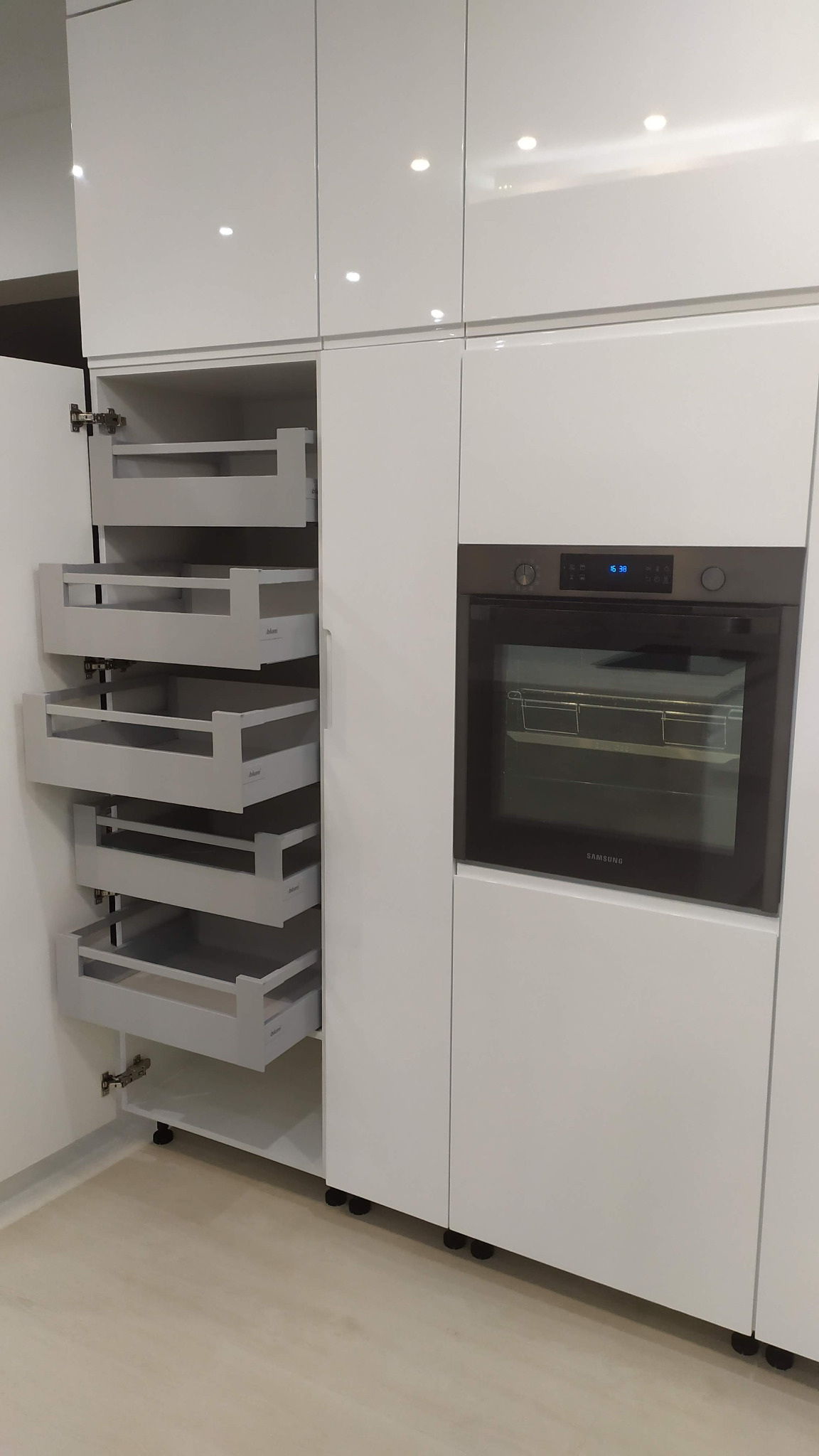 Biała, nowoczesna zabudowa kuchenna z wysuwanymi szufladami typu cargo i piekarnikiem Samsung.