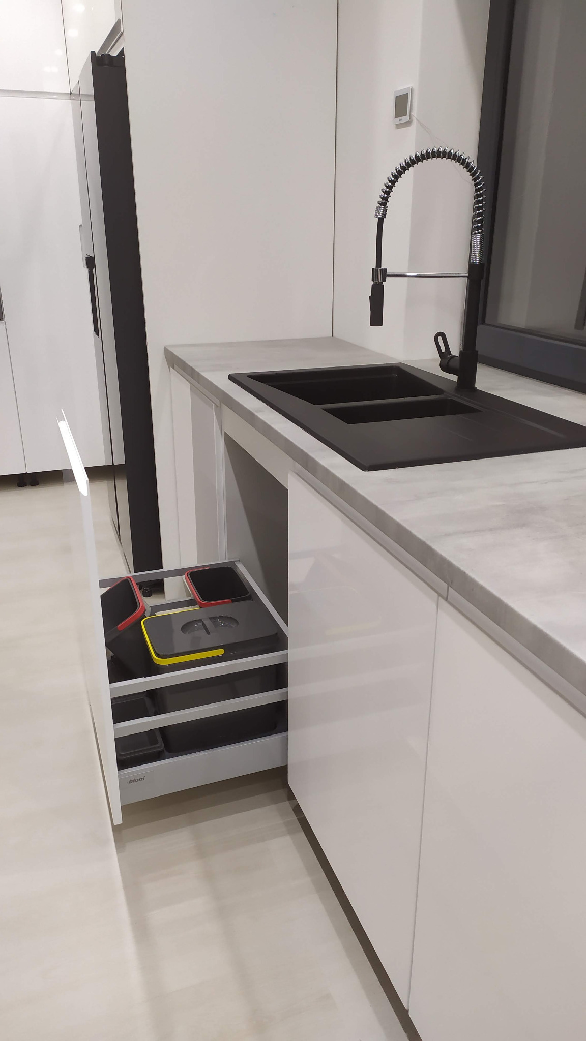 Nowoczesna kuchnia z szarym blatem, czarnym zlewem i baterią. Otwarta szuflada pod zlewem z systemem sortowania odpadów.