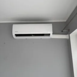 Biały klimatyzator Rotenso z wyświetlaczem temperatury (17 stopni) zamontowany na szarej ścianie, widoczna rura odprowadzająca skropliny.