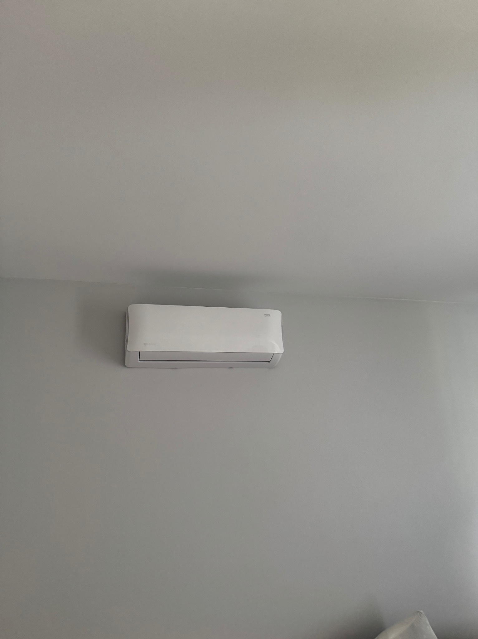 Biała klimatyzacja ścienna na szarej ścianie w minimalistycznym wnętrzu. Widok z dołu, urządzenie zamontowane pod sufitem.