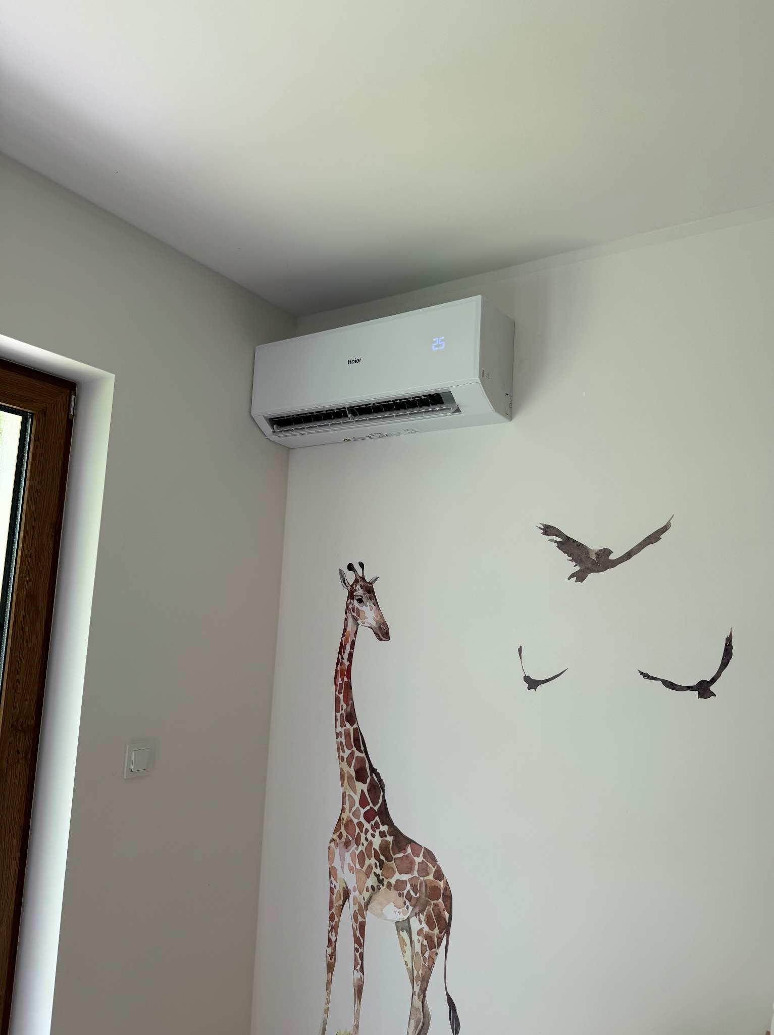 Biały klimatyzator Haier zamontowany na ścianie w pokoju dziecięcym z naklejkami żyrafy i ptaków. Usługa montażu klimatyzacji, Gniezno.