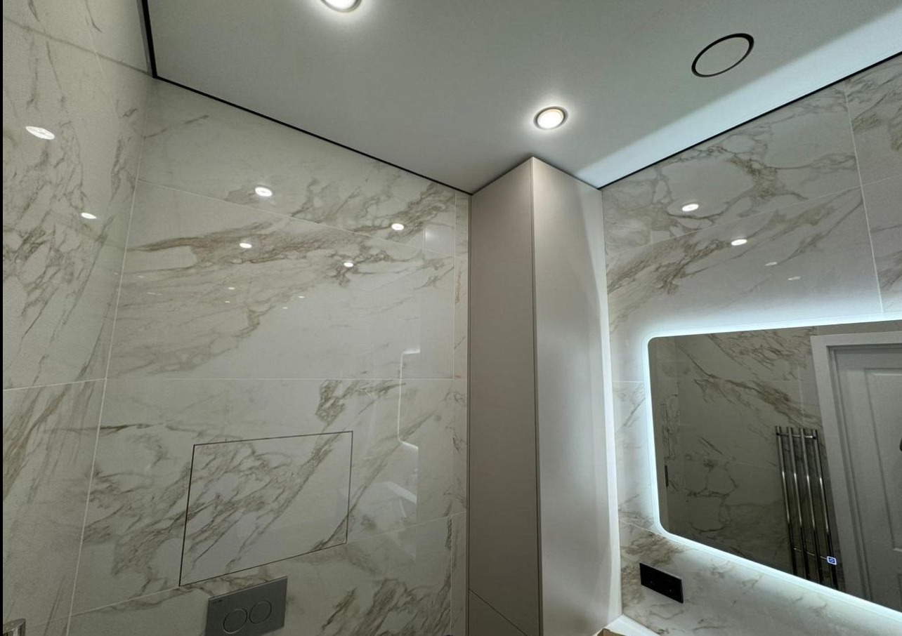 Wykończona łazienka z marmurowymi płytkami, podświetlanym lustrem i ukrytą spłuczką. Nowoczesny design z dbałością o detale i oświetlenie.