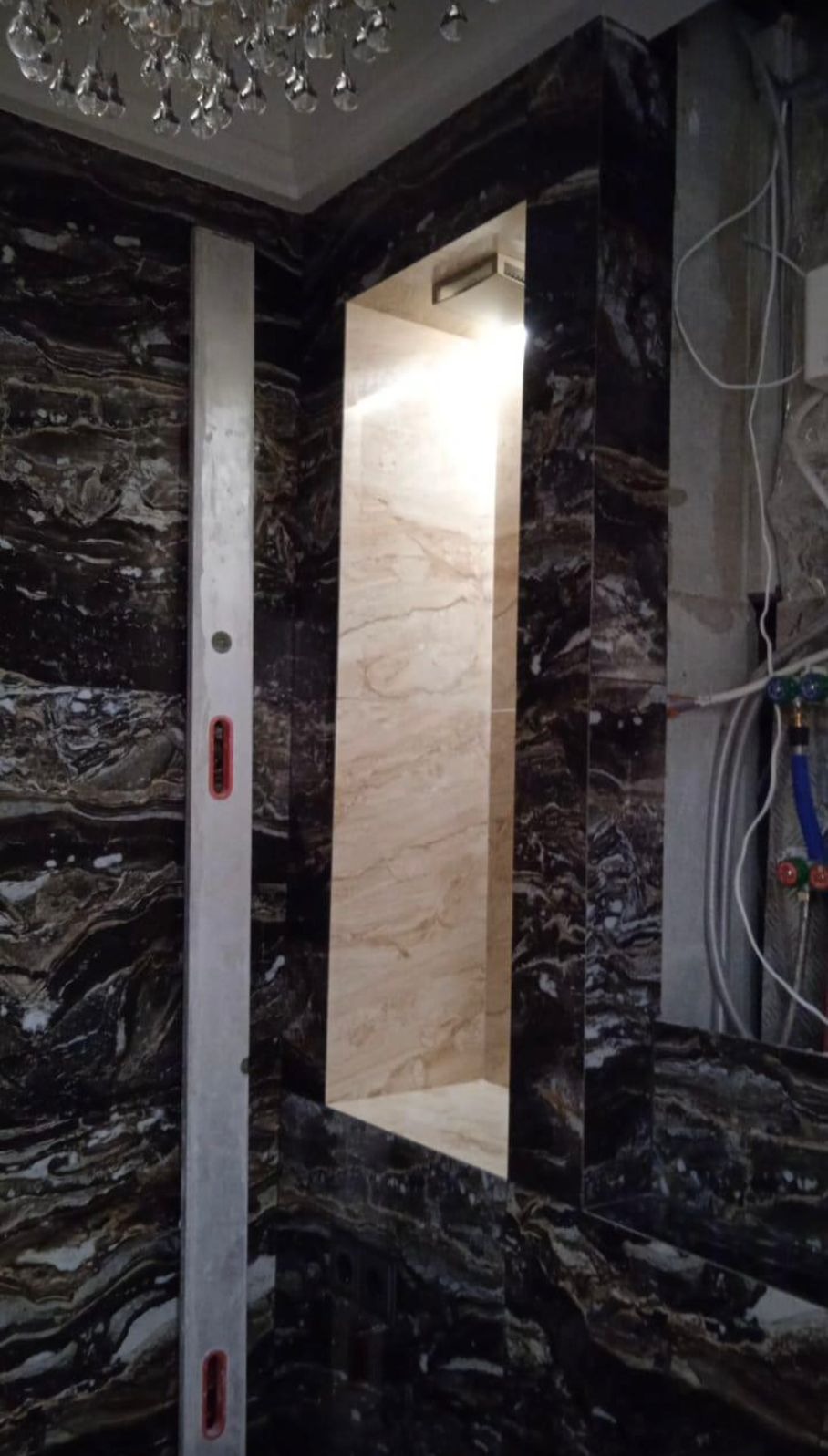 Wykończona wnęka z podświetleniem i okładziną imitującą marmur w łazience w Warszawie. Poziomica przy ścianie sugeruje precyzję wykonania.