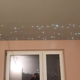 Usługi remontowo-budowlane - Szary sufit z efektem gwiazd, widoczne otwory na oświetlenie, różowe ściany, okno z widokiem na miasto w nocy, częściowo wykończone wnętrze