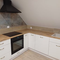 Huliailo Dmytro - Nowoczesna kuchnia na poddaszu: białe szafki z drewnianym blatem, czarna płyta i okap. Ściana wykończona płytkami w stylu vintage.
