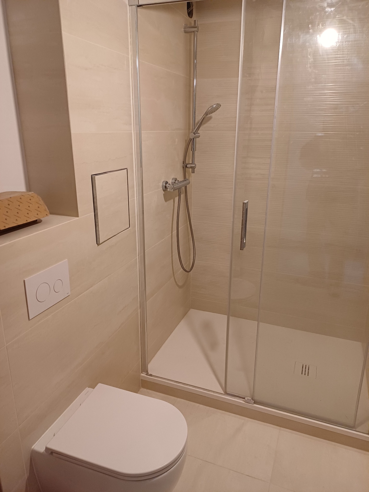 Jasna łazienka po remoncie z kabiną prysznicową z przesuwnymi drzwiami, podwieszaną toaletą i ukrytym zaworem. Na ścianie widoczny właz rewizyjny.