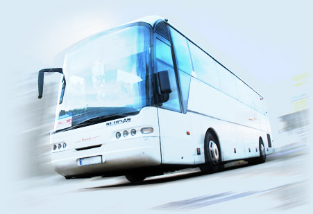 Biały autokar turystyczny w ruchu, ujęcie z lekkim efektem rozmycia, podkreślającym dynamikę jazdy.