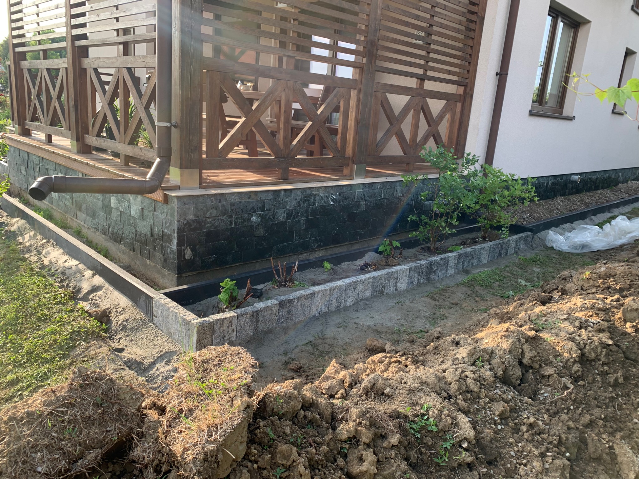 Przygotowanie terenu pod trawnik z obrzeżami betonowymi i fragmentem drewnianej altany w tle.