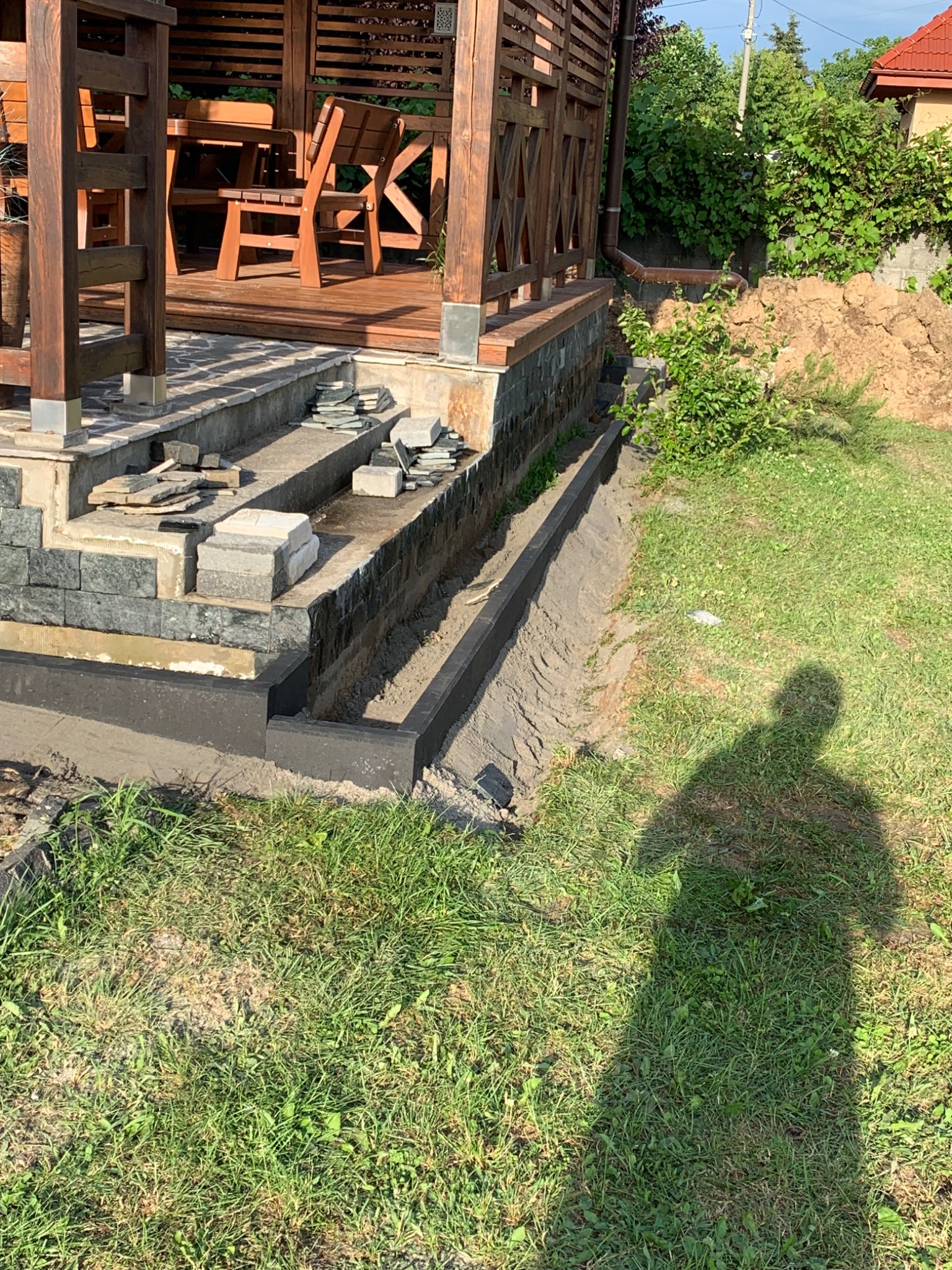 Budowa tarasu z kamiennymi schodami i obrzeżem, widoczny cień osoby fotografującej.