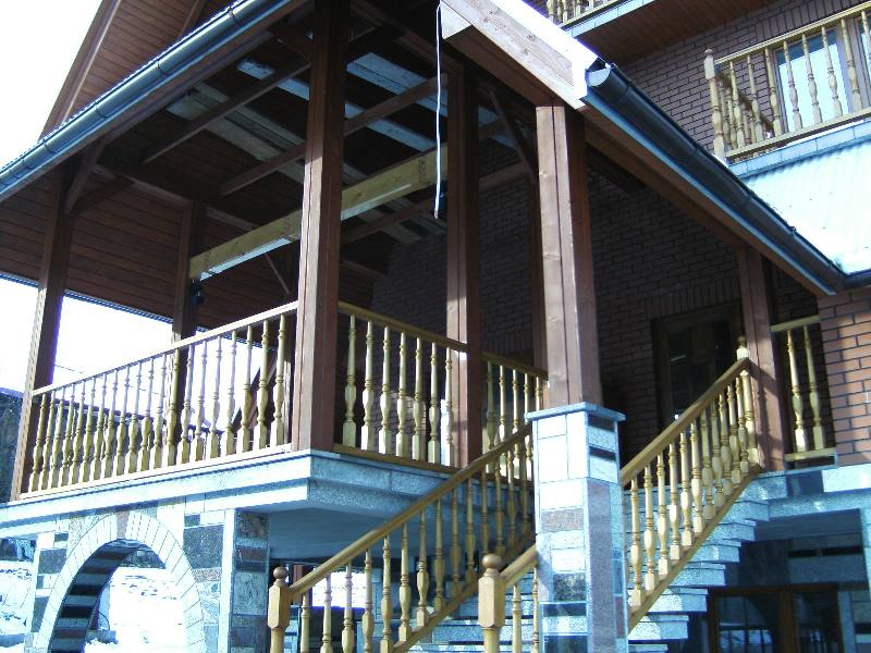 Zadaszony taras z drewnianą konstrukcją, ceglanym murem i schodami wyłożonymi kamieniem.