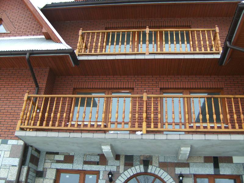 Dwupoziomowy budynek z cegły z drewnianymi balkonami z balustradami, widoczne okna i dach