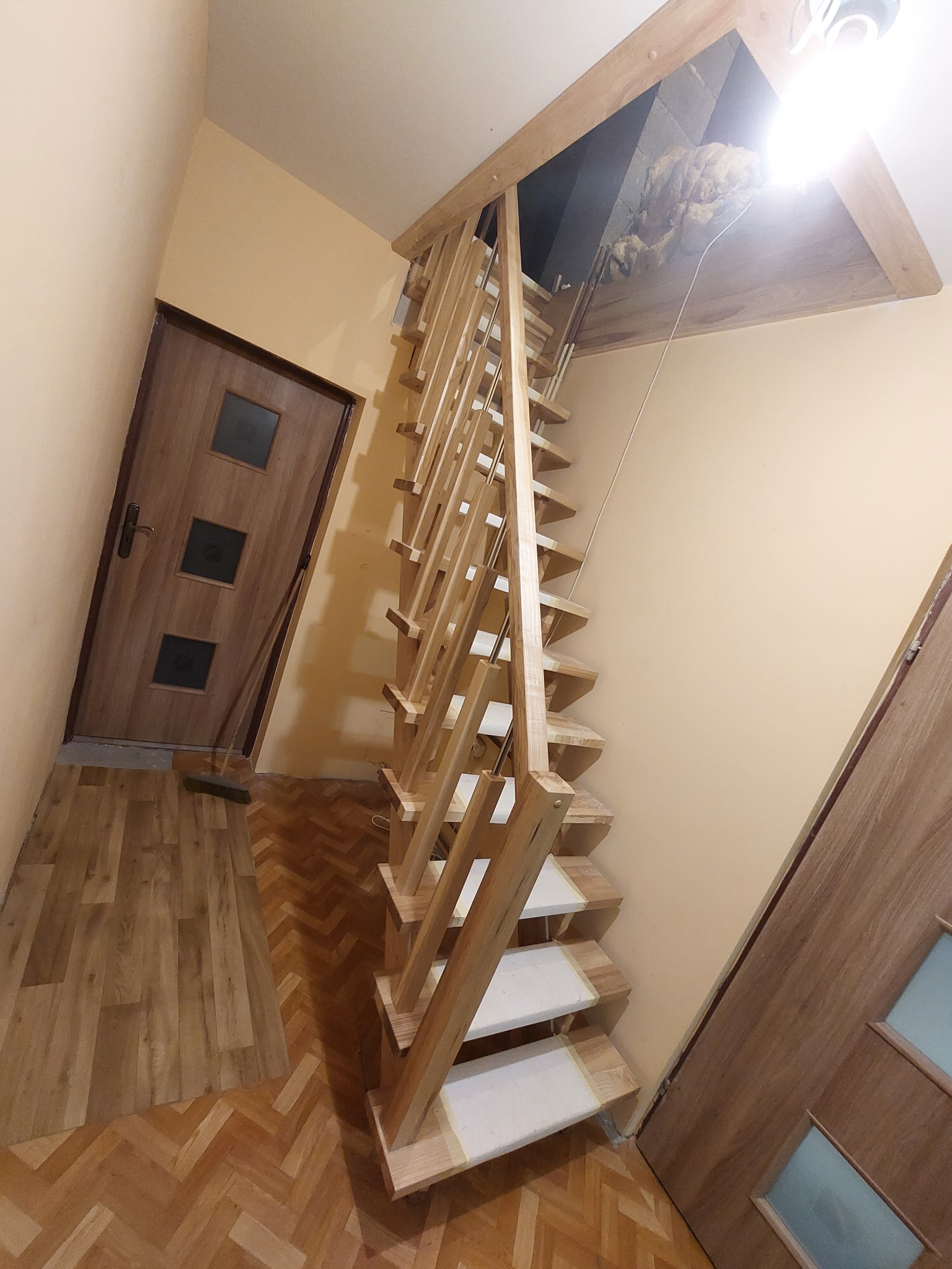 Strome, drewniane schody strychowe z ażurową balustradą prowadzą na poddasze, widok z dołu, obok drzwi z trzema szybkami i podłoga w jodełkę.