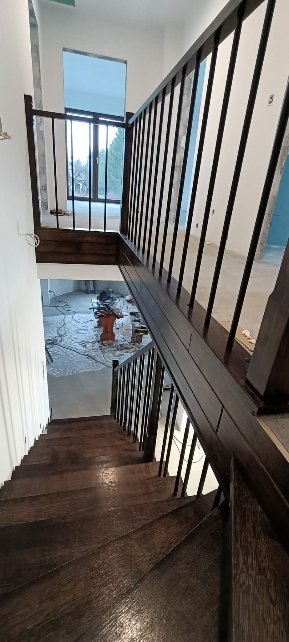 Ciemne, drewniane schody z balustradą w trakcie montażu, widoczne narzędzia i zabezpieczona podłoga w tle.