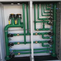 Kompleksowy system rur gazowych w szafie sterowniczej, z licznymi zaworami, czujnikami i przewodami, pomalowany na zielono z elementami mosiężnymi.