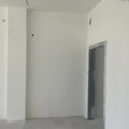 Świeżo pomalowane, białe wnętrze z zabezpieczonym folią ościeżem drzwiowym i widocznymi otworami na instalacje elektryczne.