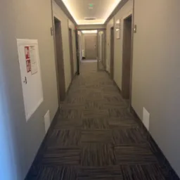 Długi korytarz w budynku w Szczercowie z teksturowanymi ścianami, wzorzystą wykładziną dywanową i oświetleniem LED w suficie.