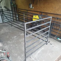 Konstrukcja z metalowych profili w warsztacie, widoczna spawarka i elementy metalowe w tle, surowy stan wykończenia.