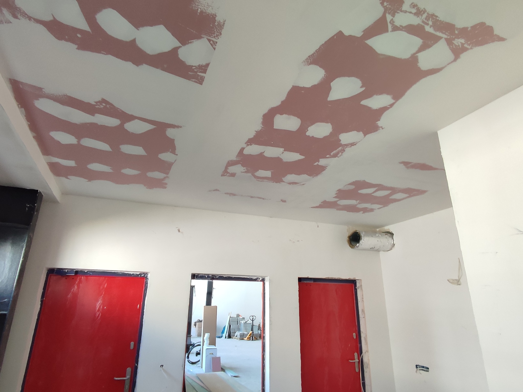 Przygotowanie sufitu: nałożona warstwa szpachli na płyty gipsowo-kartonowe, widoczne czerwone drzwi i elementy wyposażenia w tle.
