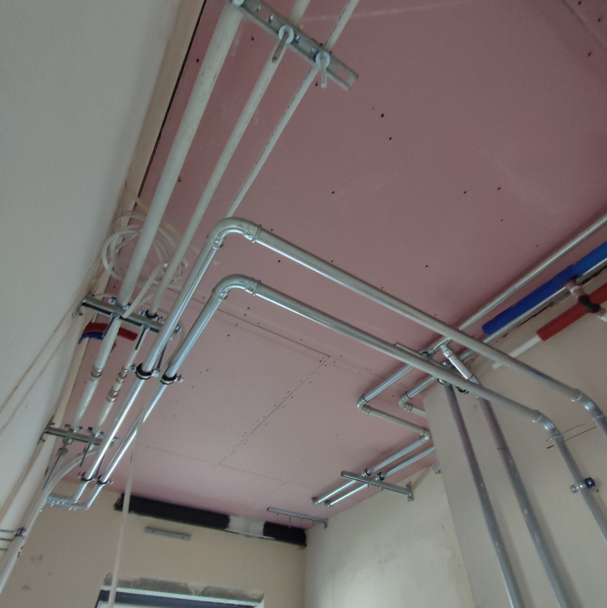 Montaż instalacji wodnej i elektrycznej pod płytą kartonowo-gipsową na suficie, widoczne metalowe rury i kable przymocowane do konstrukcji nośnej.
